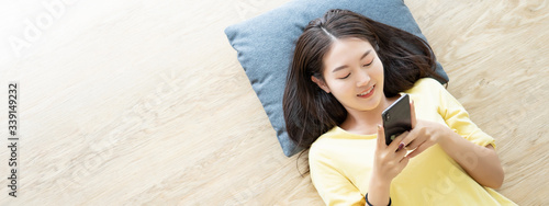 Slika na platnu Attractive young Asian woman happy lie down on wooden floor and using mobile pho