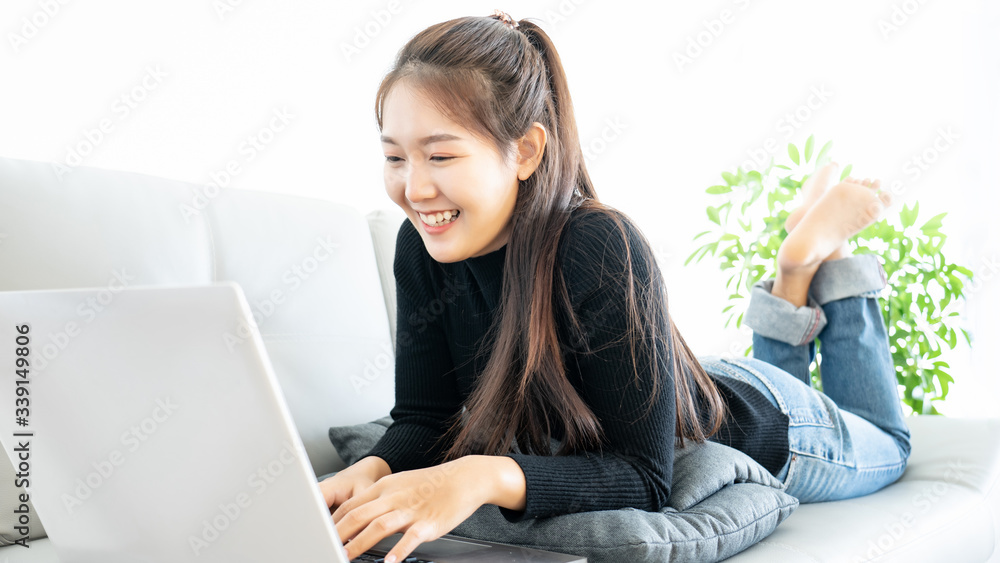 Attractive asia woman happy lying down on sofa using laptop computer connect high speed internet remote application online for work from home Attractive asia woman happy lying down on sofa using laptop computer connect high speed internet remote application online for work from home
