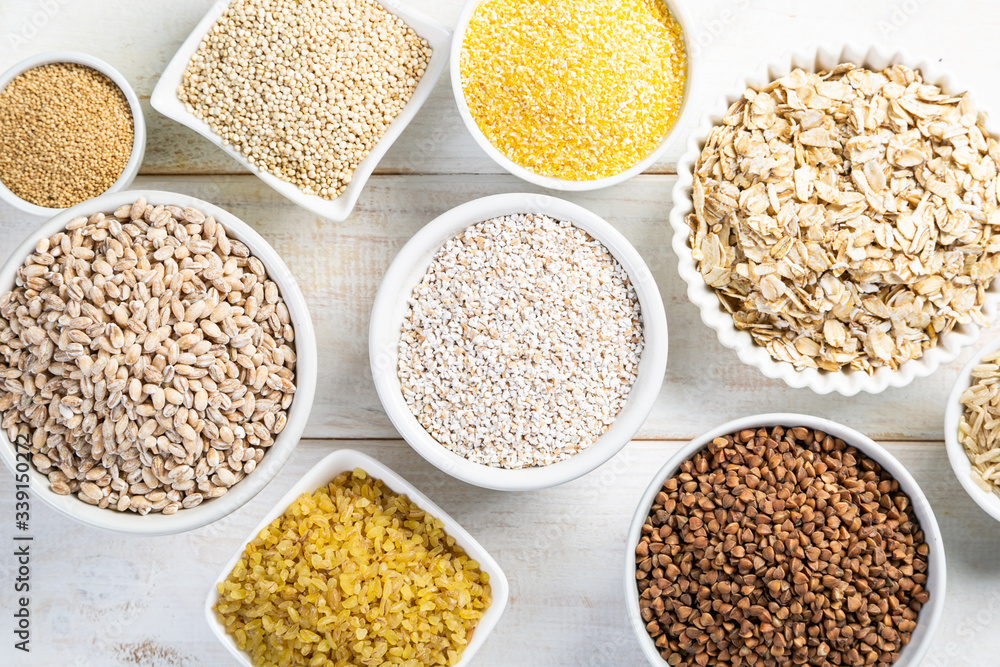 Selection of whole grains in white bowls - rice, oats, buckwheat, bulgur, porridge, barley, quinoa, amaranth, on white wood background Selection of whole grains in white bowls - rice, oats, buckwheat, bulgur, porridge, barley, quinoa, amaranth, on white wood background