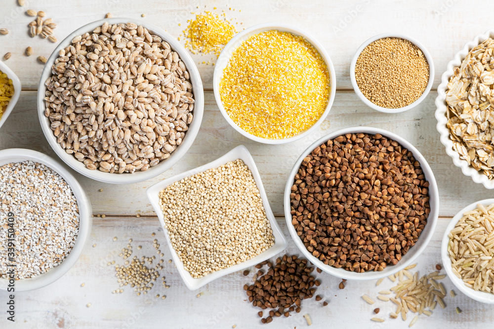 Selection of whole grains in white bowls - rice, oats, buckwheat, bulgur, porridge, barley, quinoa, amaranth, on white wood background Selection of whole grains in white bowls - rice, oats, buckwheat, bulgur, porridge, barley, quinoa, amaranth, on white wood background