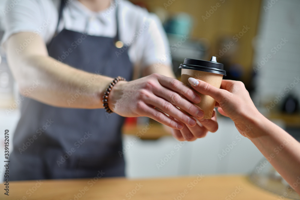 A young barista guy sells takeaway coffee and hands it to a client. Small business concept