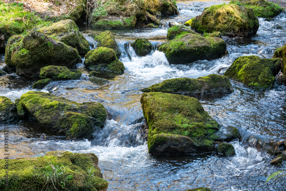 River flowing round green mossy rocks in close up River flowing round green mossy rocks in close up
