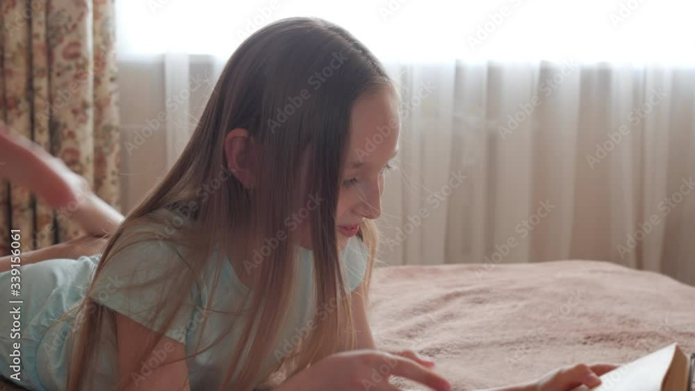Pretty girl teenager reading book lying on bed in cozy bedroom. Cute teenager girl looking book on bed in bedroom on window background. Pretty girl teenager reading book lying on bed in cozy bedroom. Cute teenager girl looking book on bed in bedroom on window background.