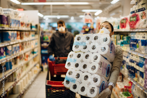 Woman couple with mask and gloves panic buying and hoarding toilette paper in supply store.Pathogen virus pandemic quarantine.Prepper buying bulk cleaning supplies due to Covid-19.Focus on the paper photo