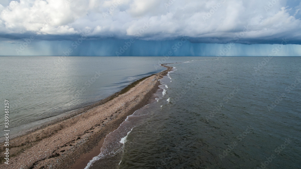 Scenic aerial view along the out stretching gravel pit in the sea bay with the dark rain and thunder clouds approaching