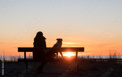 Portrait of the women, sitting on the bench, enjoying the seacoast sunset with the dog friend
