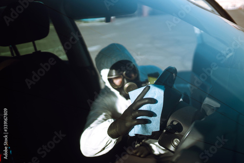 Hand of Man in protective suit washing and disinfection of the steering wheel in the car, prevent infection of Covid-19 virus, contamination of germs or bacteria. 