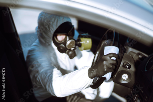 Hand of Man in protective suit washing and disinfection of the steering wheel in the car,  prevent infection of Covid-19 virus, contamination of germs or bacteria.  © maxbelchenko