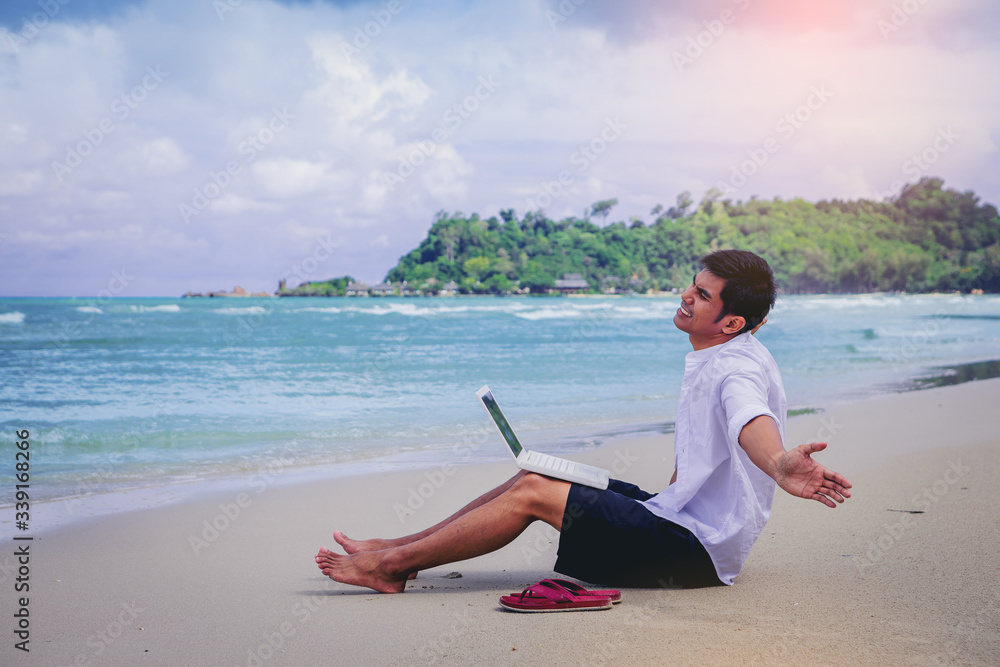 Happiness Handsome man with a shirt working with laptop sitting on the beach beside the sea. Working from home concept Happiness Handsome man with a shirt working with laptop sitting on the beach beside the sea. Working from home concept