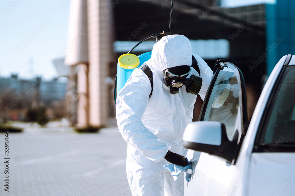 Man in protective suit washing and disinfection handles of a car, to preventing the spread of the epidemic of coronavirus, pandemic in quarantine city. Covid-19. Man in protective suit washing and disinfection handles of a car, to preventing the spread of the epidemic of coronavirus, pandemic in quarantine city. Covid-19.