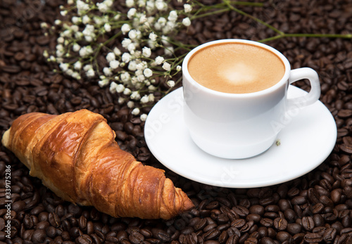 
White cup of coffee latte and croissant on a background of coffee beans