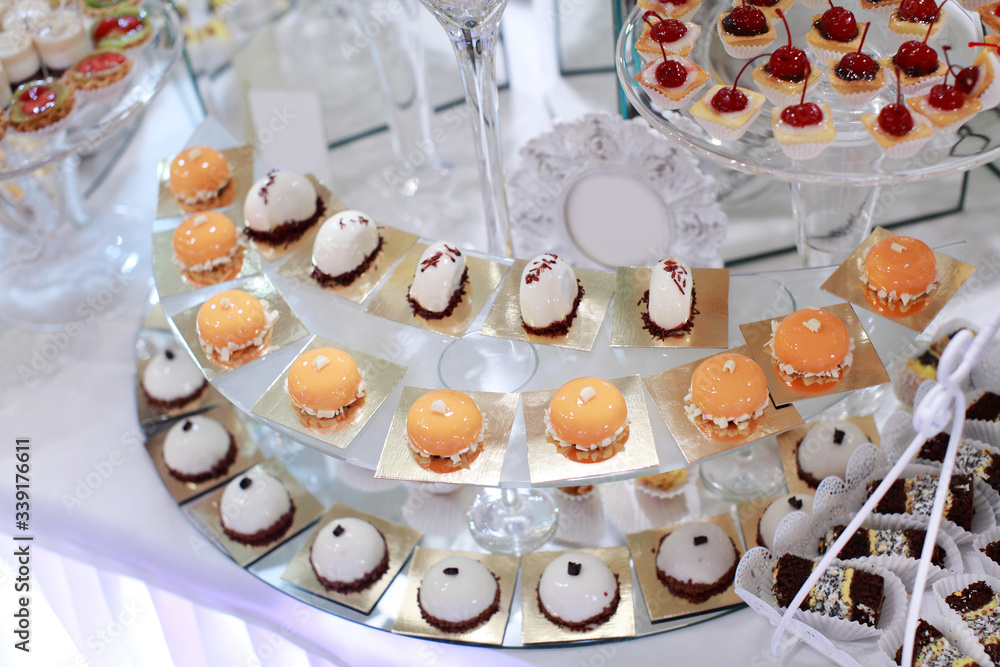 Close up of tray with lot delicious diversity pastry cakes tartlets and macaroon in a row. Fresh, multicoloured, colourful, green, yellow, white and pink sweet berry desserts, beautifully decorated Close up of tray with lot delicious diversity pastry cakes tartlets and macaroon in a row. Fresh, multicoloured, colourful, green, yellow, white and pink sweet berry desserts, beautifully decorated