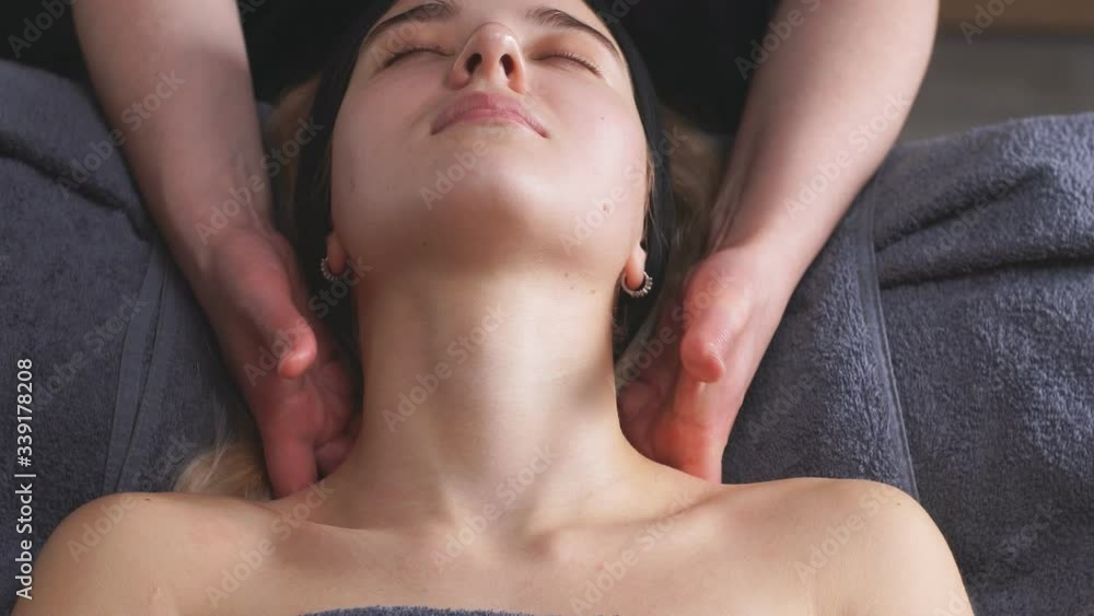 An attractive woman lies on a bed in a beauty salon and gets a massage on the decollete and neck collar area. An attractive woman lies on a bed in a beauty salon and gets a massage on the decollete and neck collar area.