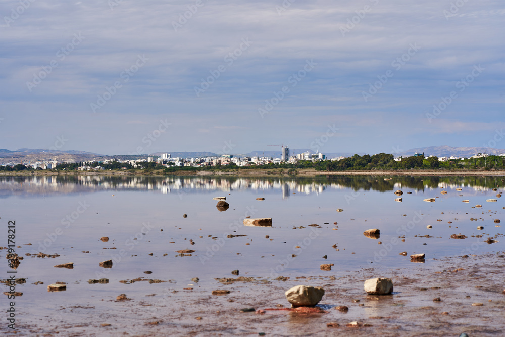 Beautiful view panoramic of a city from the shore of the salty lake Larnaca with blue sky and small clouds, reflections in the water, Larnaca, island Cyprus, deserted landscape