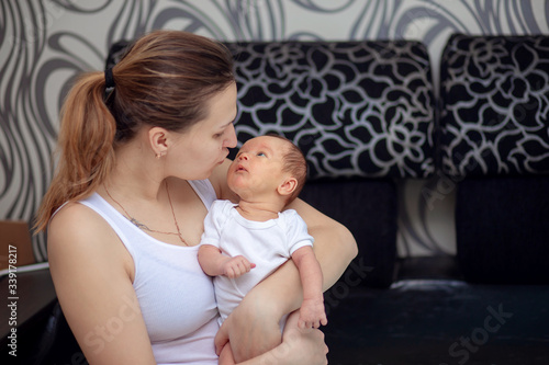 A young mother holds in her arms her newborn baby. Mom and baby are looking at each other. Mothers Day