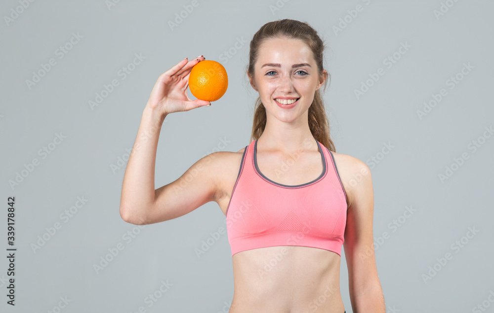 Beautiful young woman with orange fruit in hand standing on a gray background and looking at the camera. Beautiful young woman with orange fruit in hand standing on a gray background and looking at the camera.