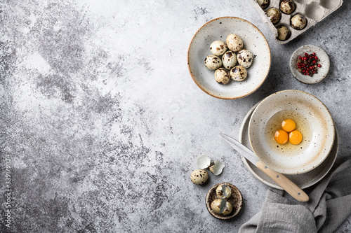 Broken quail eggs in a ceramic bowl on a gray background. Top view, place for text.