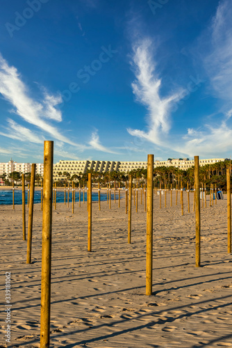On the beach of Sa Coma on the Mediterranean island of Mallorca, wooden poles for the parasols are stuck in the sand with a beautiful sunset in the background