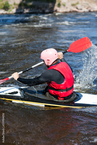A man in a pink helmet and a red vest is kayaking and rowing with a red oar. Sitting sideways. Vertical photo