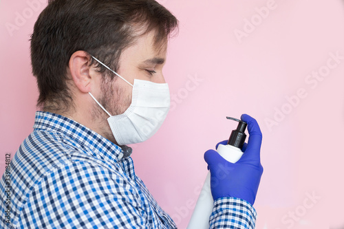 Man with sanitizing gel in his hands and wearing protective mask on pink background. Copyspace, copyplace, space for text. Coronavirus, illness, infection, quarantine, medical mask photo