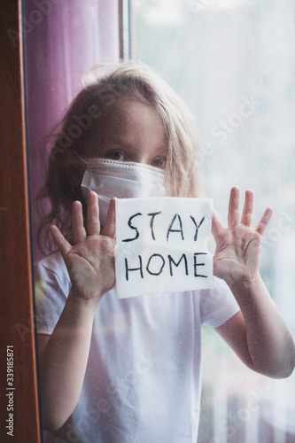 Stay at home quarantine coronavirus pandemic prevention. Sad child both in protective medical masks near windows and looks out window. View from street. Prevention epidemic. Coronavirus concept