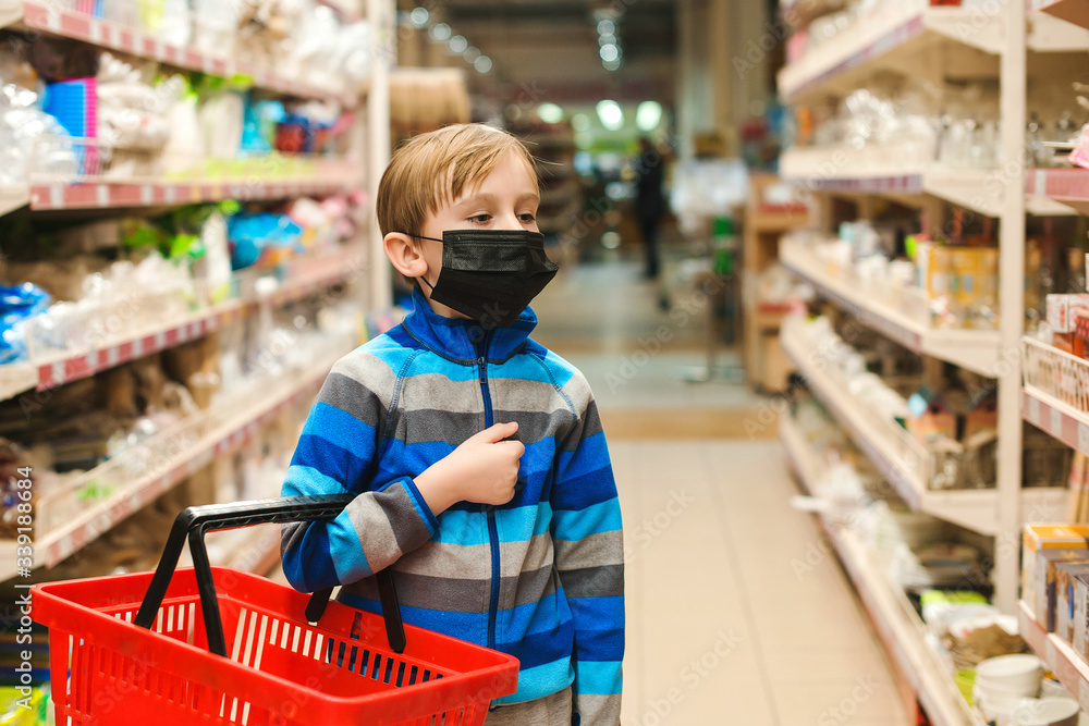 Child wears protected mask in shop. Kid with shopping basket in supermarket. Coronavirus protection.