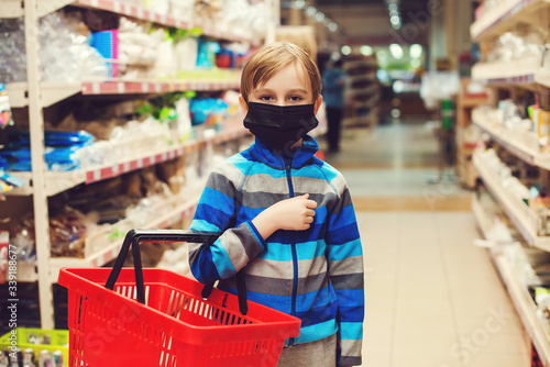 Boy in face mask in supermarket. Kid with shopping basket. Child wears protected mask in shop.