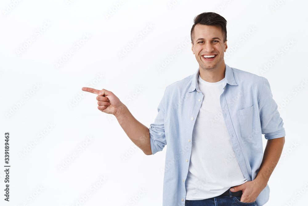Portrait of happy, handsome masculine adult man pointing finger left and smiling camera, recommend service or product, best quality item, showing way to company banner, white background Portrait of happy, handsome masculine adult man pointing finger left and smiling camera, recommend service or product, best quality item, showing way to company banner, white background