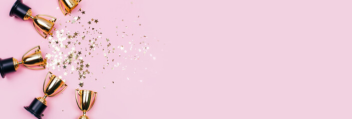 Golden winner cups with sparkles on a pink background with copy space. Festive concept. Flat lay style.