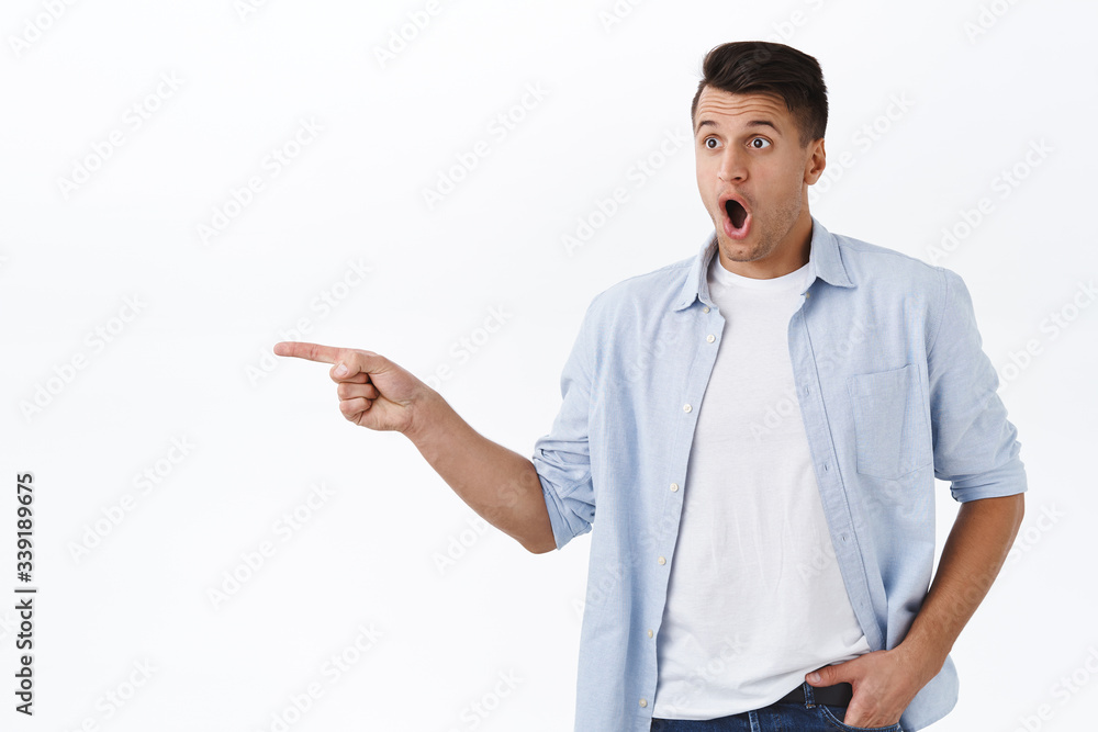 Portrait of speechless, impressed handsome caucasian guy seeing something awesome and breathtaking, gasping drop jaw and pointing finger left, showing way to cool thing, white background Portrait of speechless, impressed handsome caucasian guy seeing something awesome and breathtaking, gasping drop jaw and pointing finger left, showing way to cool thing, white background