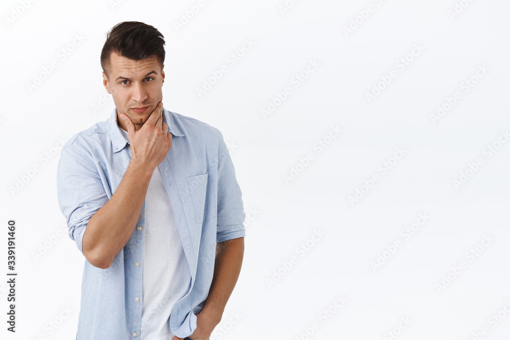 Portrait of handsome macho man, stylish haircut, touching clean shaven jawline and looking thoughtful camera, thinking, consider and making choice, pondering decision, white background Portrait of handsome macho man, stylish haircut, touching clean shaven jawline and looking thoughtful camera, thinking, consider and making choice, pondering decision, white background