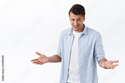 So what, why bother. Portrait of annoyed and frustrated handsome man, spread hands sideways in dismay, frowning and gasping look skeptical and scorn, standing disappointed white background