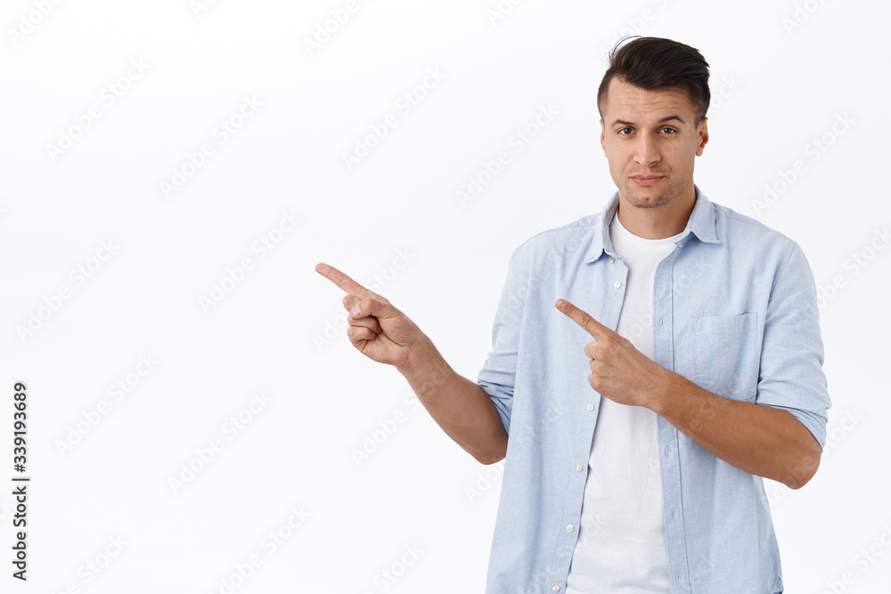 Handsome confident masculine man in shrit, pointing fingers left and look persuasive and assured camera, make final choice, recommend service, product or shopping site, white background Handsome confident masculine man in shrit, pointing fingers left and look persuasive and assured camera, make final choice, recommend service, product or shopping site, white background