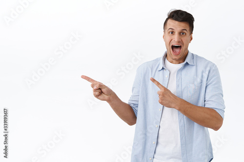 Portrait of excited, enthusiastic handsome man pointing fingers left and smiling amazed, found excellent promo, best offer in stock, special discount just click link, white background