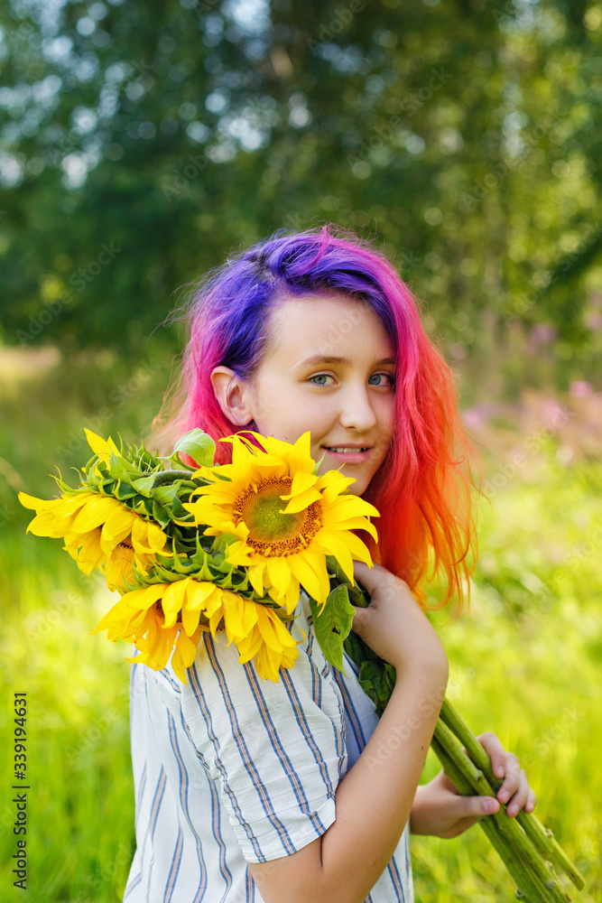 Pink and lilac strands of hair. A beautiful happy teenage girl with a sunflower enjoys nature and laughs on a summer field. The sun's glare, the sun's rays, the sun's radiance. Illuminated Pink and lilac strands of hair. A beautiful happy teenage girl with a sunflower enjoys nature and laughs on a summer field. The sun's glare, the sun's rays, the sun's radiance. Illuminated