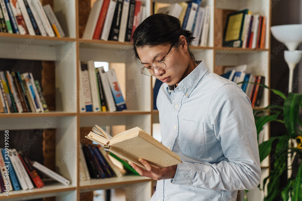 Image of serious handsome asian man in eyeglasses reading book Image of serious handsome asian man in eyeglasses reading book