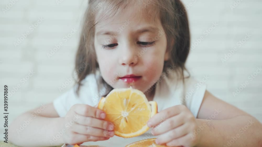 Kids in self-isolation. A little girl eating orange. A child is sitting at home. Cute girl. Healthy fresh food. Strengthening of immunity. Quarantined Family. Close-up. Kids in self-isolation. A little girl eating orange. A child is sitting at home. Cute girl. Healthy fresh food. Strengthening of immunity. Quarantined Family. Close-up.
