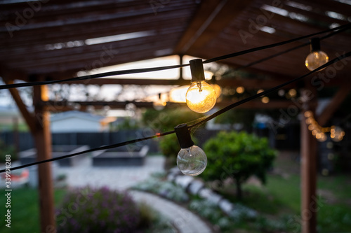 String lights under a pergola in a backyard at sunset.