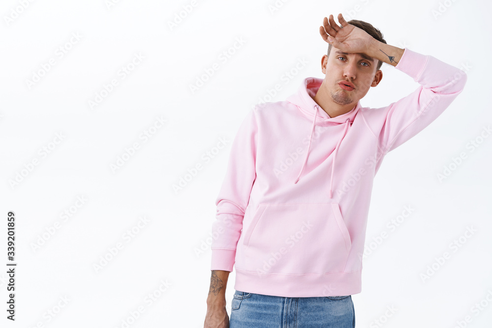Portrait of relieved young tired blond man, got rid of terrible situation, sighing and wiping sweat from head, feel fatigue or hot in hoodie on summer warm weather, standing white background Portrait of relieved young tired blond man, got rid of terrible situation, sighing and wiping sweat from head, feel fatigue or hot in hoodie on summer warm weather, standing white background