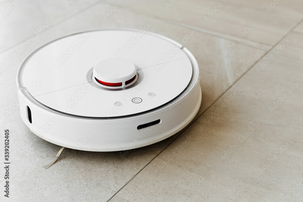 Robot vacuum cleaner during cleaning,white robot vacuum cleaner cleans the floor from debris,home cleaning with an electric vacuum cleaner,vacuum cleaner electric robot cleaning technology Robot vacuum cleaner during cleaning,white robot vacuum cleaner cleans the floor from debris,home cleaning with an electric vacuum cleaner,vacuum cleaner electric robot cleaning technology