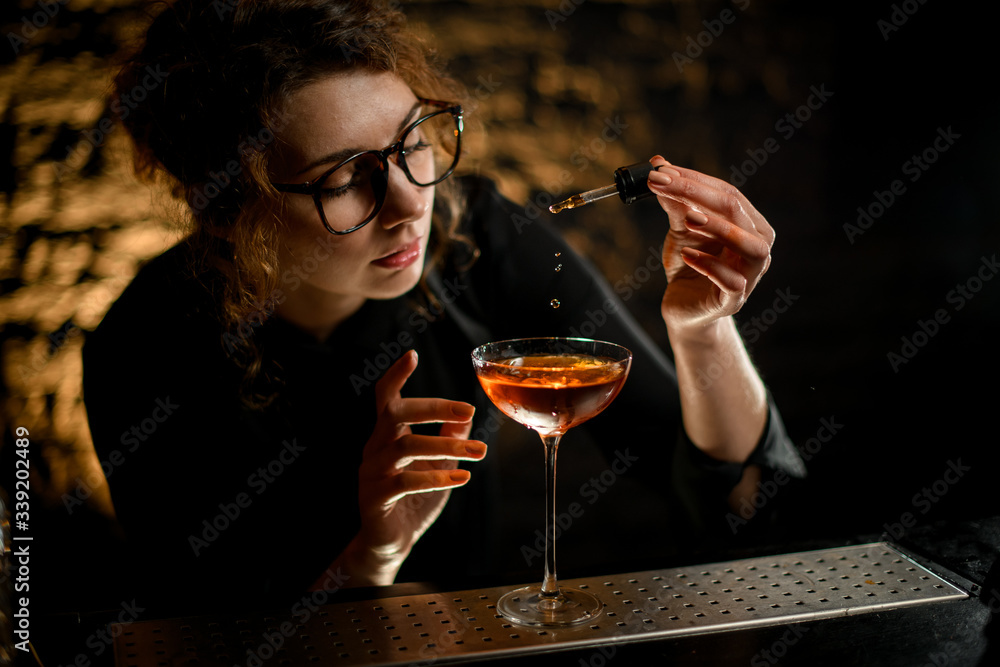 beautiful woman at bar attentively adds ingredient to glass with drink