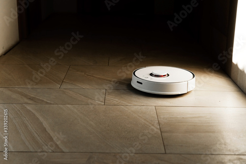 Robot vacuum cleaner during cleaning,white robot vacuum cleaner cleans the floor from debris,home cleaning with an electric vacuum cleaner,vacuum cleaner electric robot cleaning technology