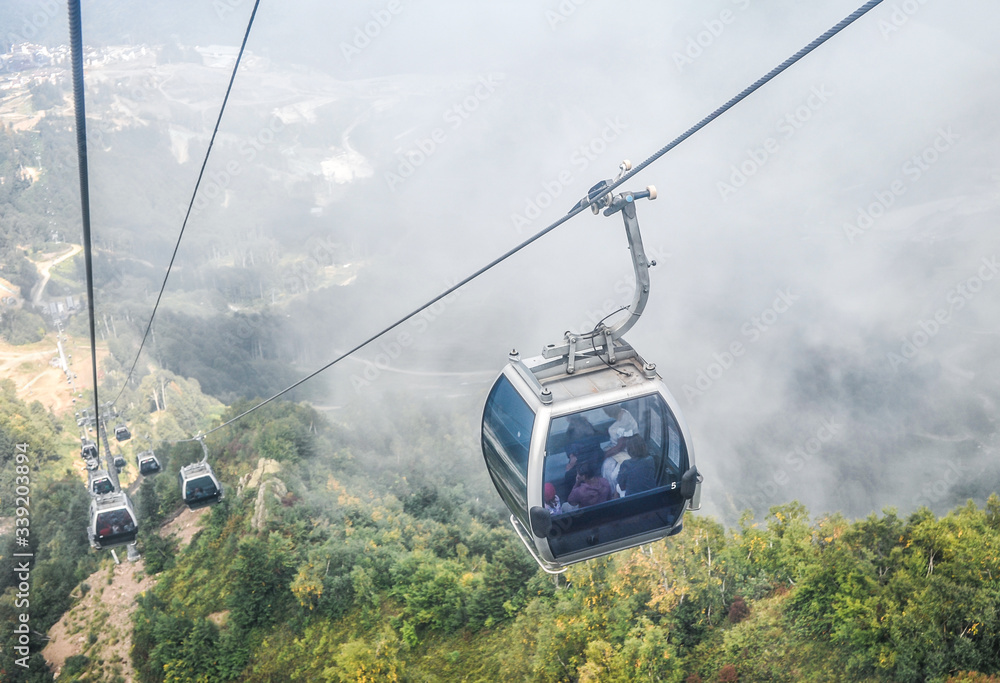 Cableway and closed glass cabins high in the mountains against the backdrop of clouds and forest