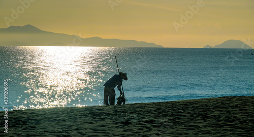 Along the shores of Hoi An, Cua Dai beach in Vietnam, with a lot of best luxury hotels and resorts. Silhouette of a worker with typical conical hat cleaning the sandy beach.