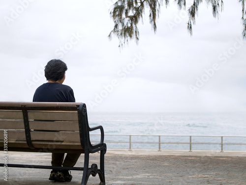 Woman sitting alone on a bench by the sea, back view, copy space