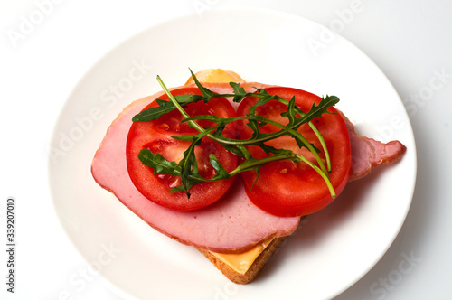 Sandwich of sturgeon, cheese, bread, tomatoes and arugula on a white background on a plate view from the top