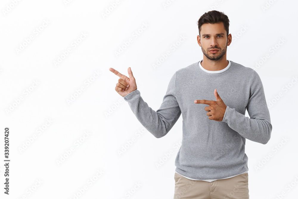 Serious-looking confident and sassy masculine macho man with bristle in modern grey sweater over t-shirt, pointing left look determined and motivated camera, persuade turn your attention to product Serious-looking confident and sassy masculine macho man with bristle in modern grey sweater over t-shirt, pointing left look determined and motivated camera, persuade turn your attention to product