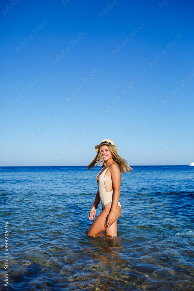 Sexy, cheerful, light, cheerful, fair-haired girl in a hat, in a beige swimsuit. Sandy beach, cliffs, vacation at sea. Sexy, cheerful, light, cheerful, fair-haired girl in a hat, in a beige swimsuit. Sandy beach, cliffs, vacation at sea.