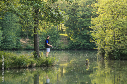 Man fishing in the green wilderness with lush forest on a sunny summer day at sunset.