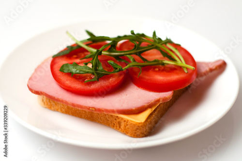 Sandwich of balyk, cheese, bread, tomatoes and arugula on a white plate on a plate view from the side